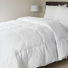 a white comforter on a bed in a room with a nightstand and lamp next to it