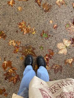 a person standing on the ground with their feet up in front of some leaves and a bag