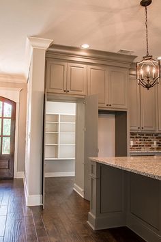 an empty kitchen with wood floors and white cabinets in the center, along with a chandelier hanging from the ceiling