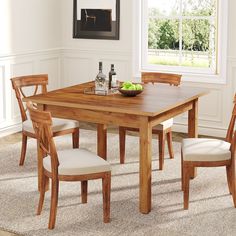 a wooden table with four chairs and a bowl of fruit on it in front of a window