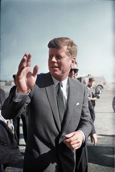 a man in a suit and tie is holding his hand up to the camera while others look on