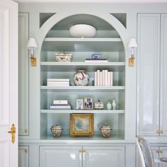 a white bookcase filled with lots of books next to a wall mounted light fixture