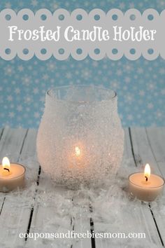 frosted candle holder sitting on top of a wooden table next to two lit candles