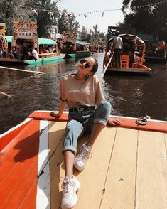 a woman sitting on the edge of a boat in front of other boats floating down a river