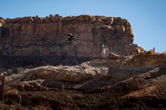 a man flying through the air while riding a motorcycle in front of a rocky mountain