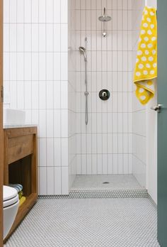 a white tiled bathroom with yellow towels hanging on the shower door and toilet in the corner