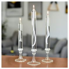 three glass candlesticks sitting on top of a wooden table next to a couch