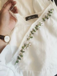 a person holding onto a white shirt with green leaves on it and a watch in their hand