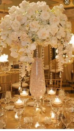 a vase filled with white flowers sitting on top of a table covered in wine glasses