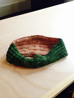 a knitted green and brown bowl sitting on top of a wooden table next to a window