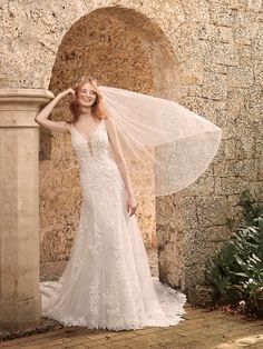 a woman in a wedding dress standing next to a stone wall and wearing a veil