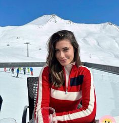 a woman sitting at a table in front of a snow covered mountain with skis on it