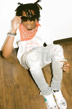 a young man sitting on the floor with his hand to his ear and wearing sunglasses