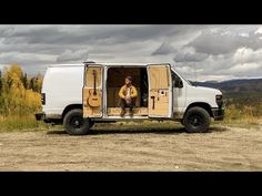 a man sitting in the back of a white van on top of a dirt road