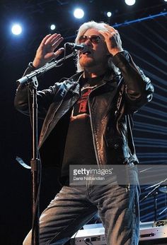 a man standing on stage with his hands in the air while holding a microphone to his ear