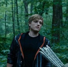 the young man is holding arrows in his hands while standing in the woods with trees behind him