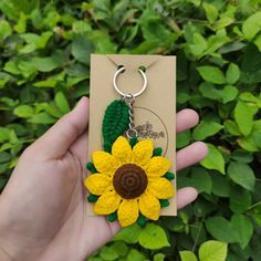 a hand holding a keychain with a yellow and green flower attached to it