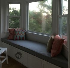 a window seat with pillows on it in front of the windowsill and trees outside