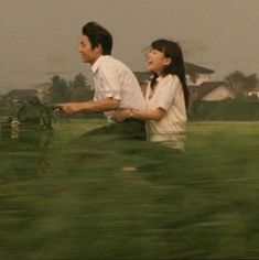 a man and woman walking through a lush green field