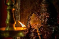 a candle is lit in front of an intricately carved ganeshi idol, which sits next to a brass oil lamp