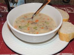 a white bowl filled with soup next to two pieces of bread on a red and white place mat