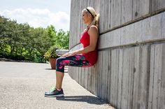 a woman sitting on the side of a building next to a wall holding a cup