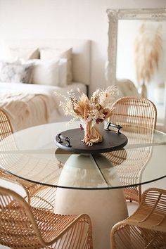 a glass table with wicker chairs around it and a vase filled with flowers on top