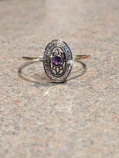 a close up of a ring on a stone surface with an oval shaped purple stone in the center