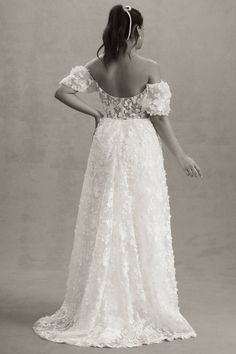 a woman in a white dress with flowers on her shoulder and back, looking off to the side