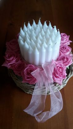 a basket filled with white candles and pink roses on top of a wooden table next to a ribbon