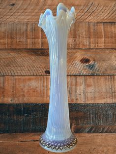 a white glass vase sitting on top of a wooden table next to a wood wall