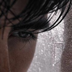 a woman's eye with water droplets on the window behind her, close up