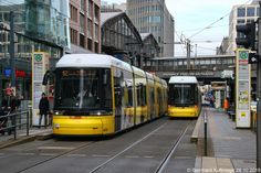 two yellow and white trains on tracks next to each other in the middle of a city