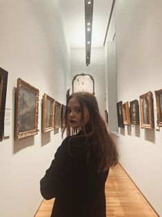 a woman is standing in an art gallery looking at pictures on the wall and taking a selfie