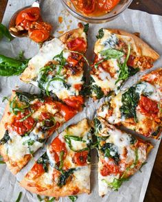 a pizza with spinach, tomatoes and cheese cut into slices on a piece of parchment paper