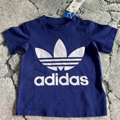 New With Tags Snap Side Buttons On Shoulder Adidas Original Classic 100% Cotton Blue Crew Neck T-shirt For Playwear, Blue Short Sleeve T-shirt For Playwear, Blue Letter Print Top For Playwear, Blue Tops With Letter Print For Playwear, Adidas Casual Tops For Playwear, Casual Adidas Tops For Playwear, Adidas Navy Short Sleeve Tops, Adidas Blue Tops With Logo Print, Navy Short Sleeve Playwear Top