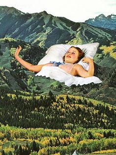 a woman laying on top of a bed in the middle of a forest with mountains behind her