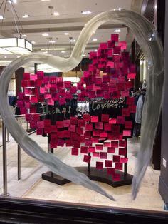 a heart made out of red and white sticky notes in a store window with the word love spelled on it