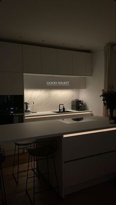 a white kitchen with an island counter and bar stools in front of the sink