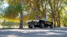 an old black car is parked on the side of the road in front of some trees