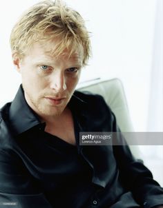 a man with blonde hair sitting in a chair looking off to the side, wearing a black shirt