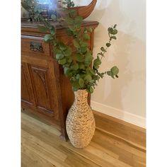 a vase filled with green leaves sitting on top of a wooden floor next to a mirror