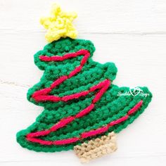 a crocheted christmas tree ornament hanging on a white wooden wall with red, yellow and green yarn