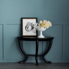 a vase with flowers sitting on top of a table next to a framed photo and an art piece