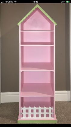 a pink bookcase with a green roof and white picket fence on the bottom shelf