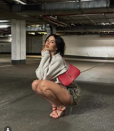 a woman kneeling on the ground holding a red purse in her right hand and looking up