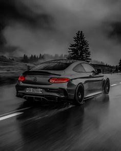 a black and white photo of a car driving down the road with dark clouds in the background