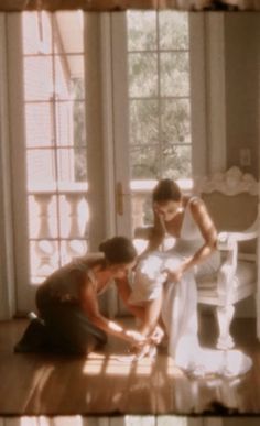 two women in white dresses standing next to each other on a hard wood floor with windows