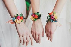 two brides holding hands with colorful flowers on their wristbands and wearing matching bracelets