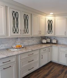 a kitchen with white cabinets and marble counter tops